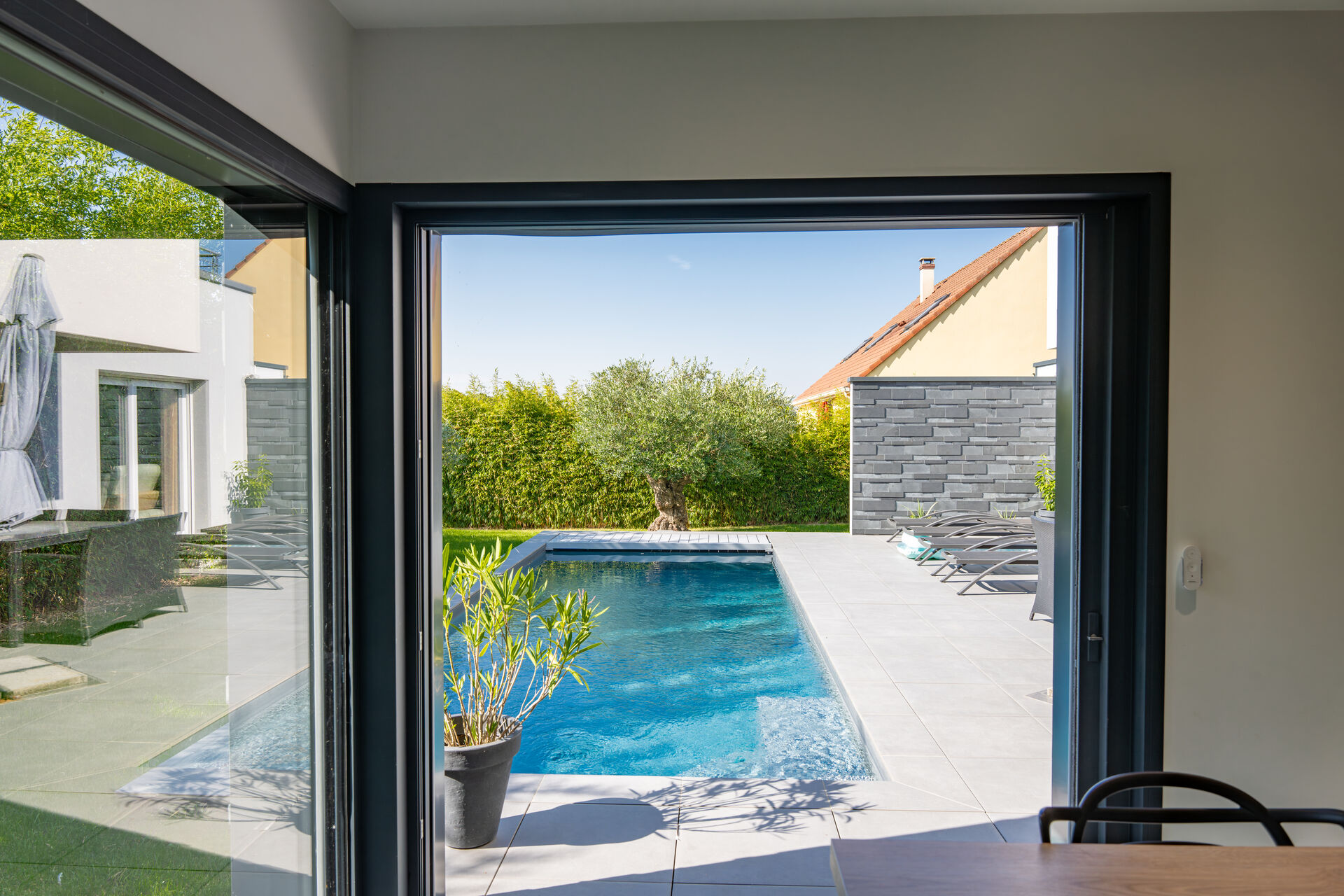 Porte-fenêtre aluminium ouverte sur une terrasse et une piscine